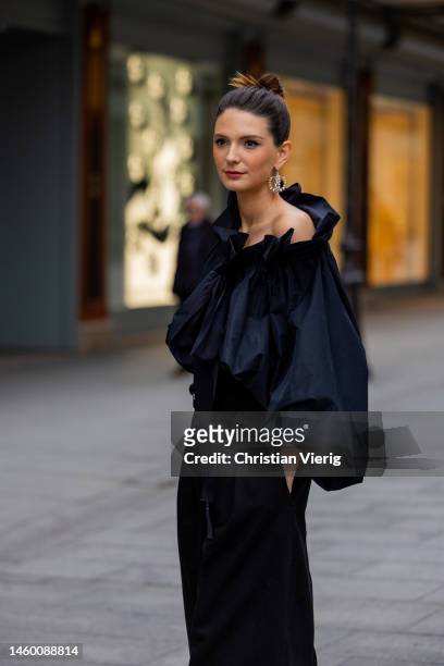 French actress Josephine Japy wears black asymmetric ruffled blouse with puffy long sleeves, black high waist pants, pearl earring, heels sandals...