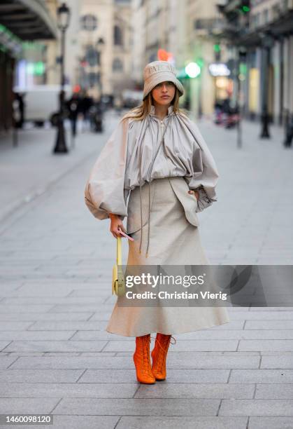 Carla Ginola wears grey creme white bucket hat with logo print, pleated blouse with wide sleeves, high waisted maxi skirt, orange laced pointed ankle...