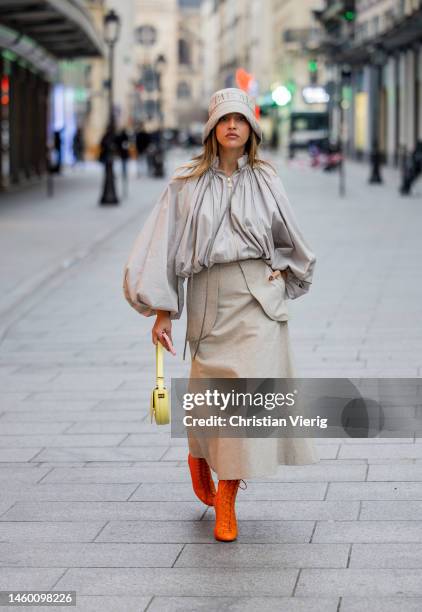 Carla Ginola wears grey creme white bucket hat with logo print, pleated blouse with wide sleeves, high waisted maxi skirt, orange laced pointed ankle...