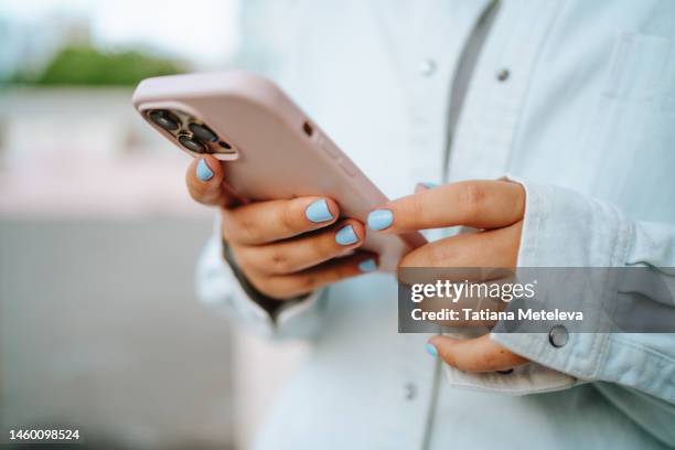 close up female hands with blue manicure using pink smartphone outdoors - obscured face phone stock pictures, royalty-free photos & images