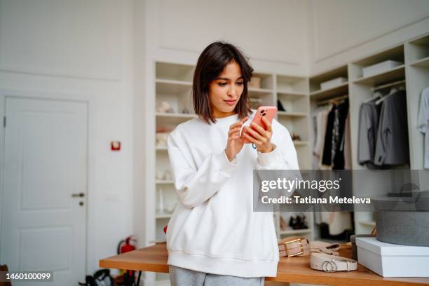 thrift store retail sales. concentrated brunette female using smartphone in wardrobe of clothes shop - brand name mobile payment photos et images de collection