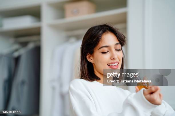 toothy smiling woman spraying and testing perfume oil water on her wrist - aroma foto e immagini stock