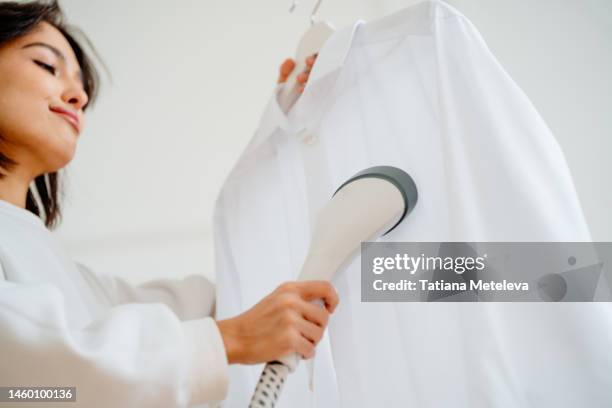 woman using steamer machine equipment for removing wrinkles and folds on clothes - woman chores stock pictures, royalty-free photos & images