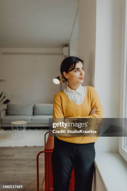 porträt einer lächelnden geschäftsfrau, die durch das fenster in ihrem büro schaut - neben stock-fotos und bilder