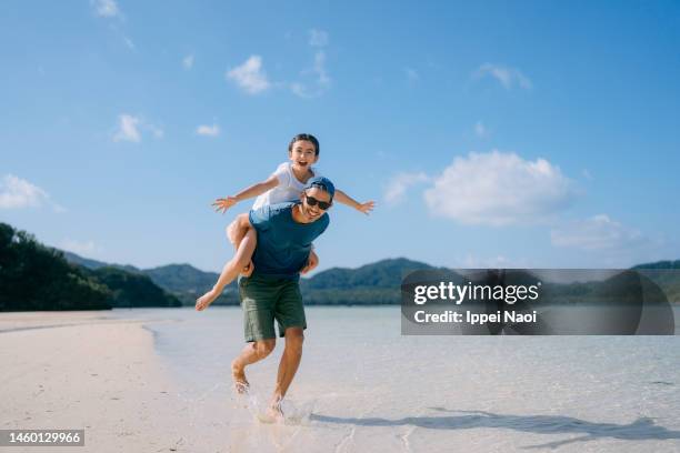 father giving piggyback ride to young daughter on beach, japan - asian father stock pictures, royalty-free photos & images