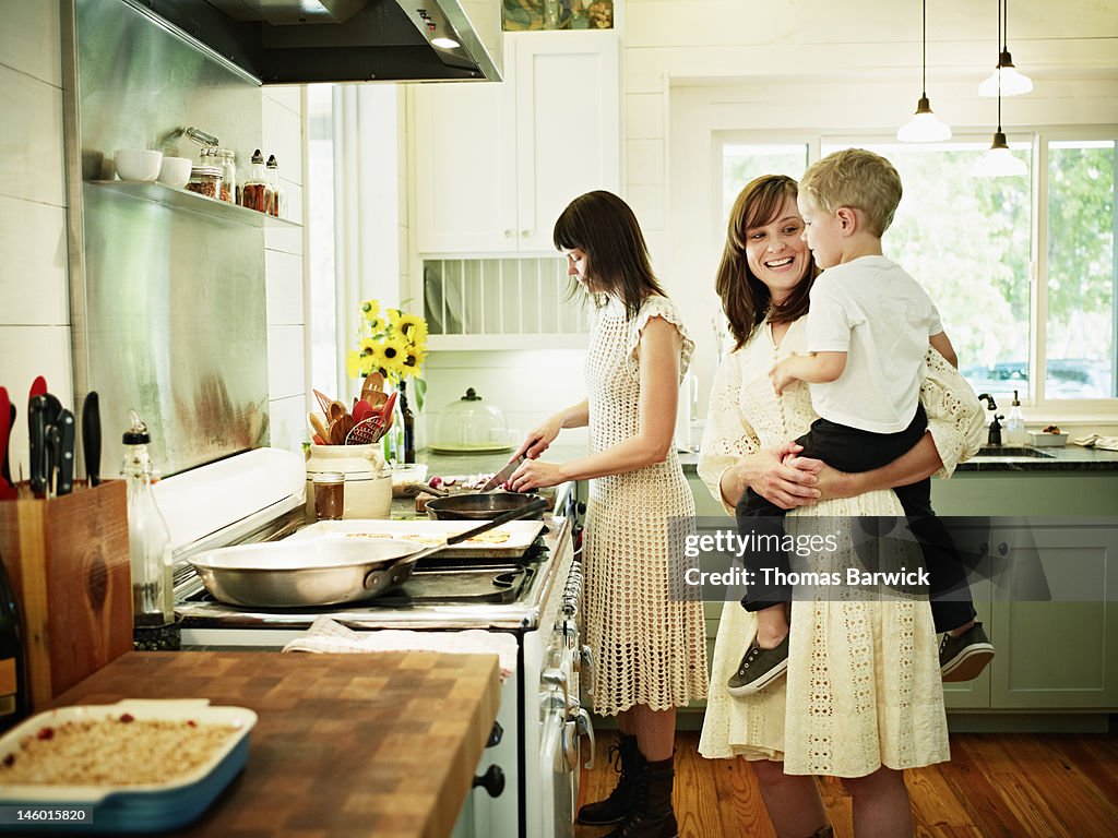 Mother cooking in kitchen while aunt holds nephew