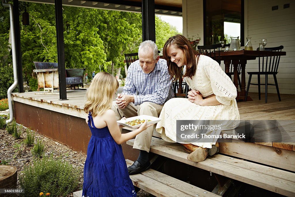 Young girl offering appetizers to family on porch