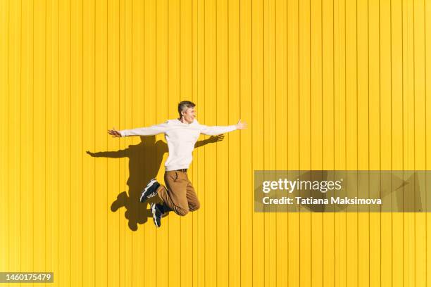 young man in casual cloth jumping on yellow wall background. - best male dancer stock pictures, royalty-free photos & images