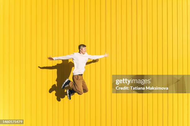 young man in casual cloth jumping on yellow wall background. - colour street dance stock pictures, royalty-free photos & images