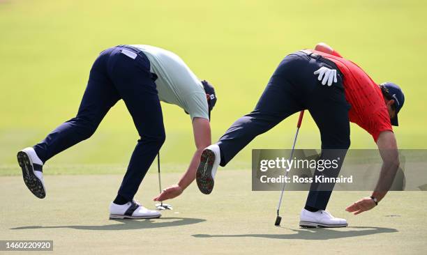 Scott Jamieson of Scotland and Patrick Reed of The United States clear sand from the 1st hole green during the continuation of Round Two on Day Three...