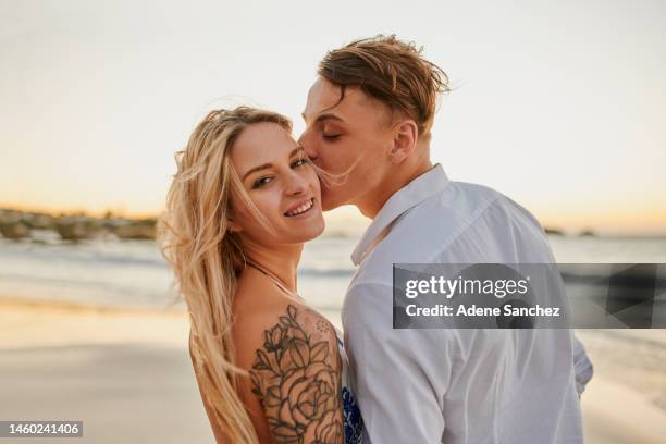 strand, liebe und mann, der seine frau im urlaub, wochenendtrip oder abenteuer auf die wange küsst. porträt, romantik und junger mann mit zuneigung für frau am meer oder meer während des urlaubs in australien. - couple kissing stock-fotos und bilder