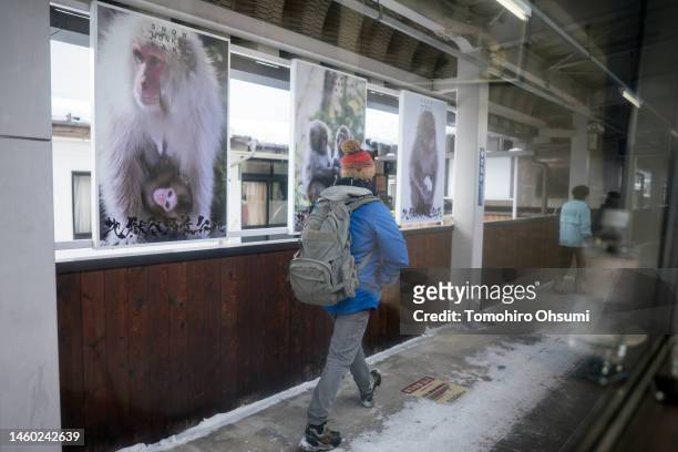 Tourist walks past advertisements of Jigokudani Yaen-koen wild macaque monkey park, seen from a train window on January 28, 2023 in Yamanouchi,...