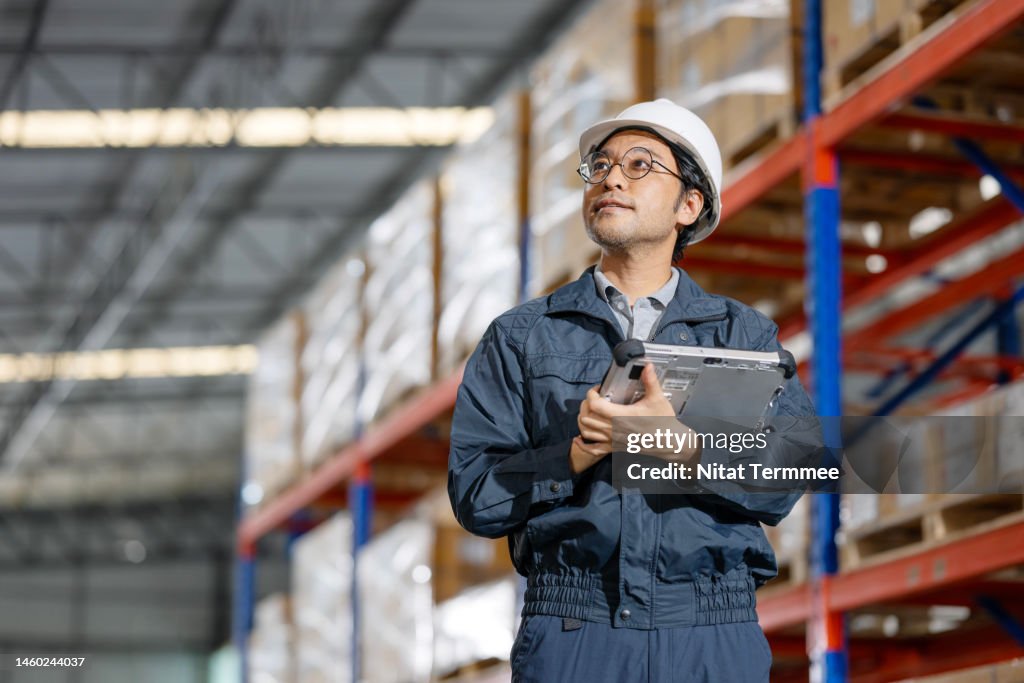 On-time Delivery is Our Service to Support Your Business. Low-angle view of a Japanese warehouse owner using a digital tablet while working in a logistics warehouse.