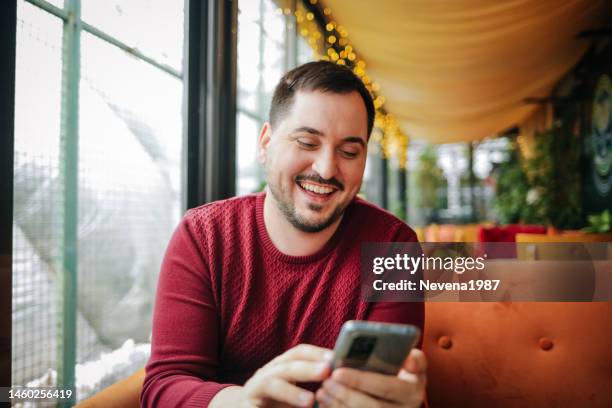 young smiling man sitting in coffee shop and using phone - 1987 25-35 stock pictures, royalty-free photos & images