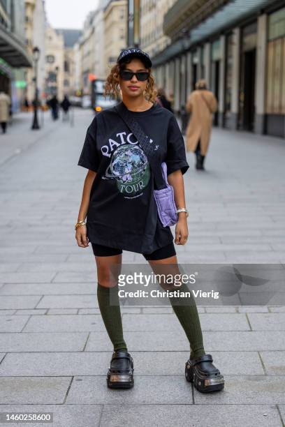 Paola Locatelli wears black shirt with graphic print, cap, purple bag, leggings shorts, knee high green socks, Balenciaga shoes outside Patou at La...
