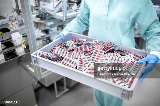 a worker in protective gear carefully carries a container filled with blister-packaged capsules - pharmaceutical compounding stock pictures, royalty-free photos & images