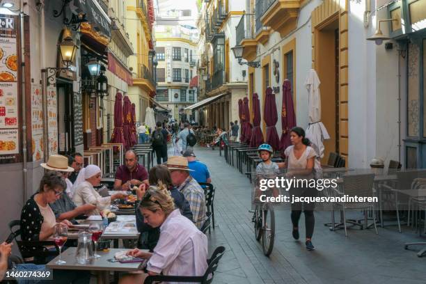 street life in seville, spain, including some people eating on a terrace and a woman with a bicycle - seville food stock pictures, royalty-free photos & images