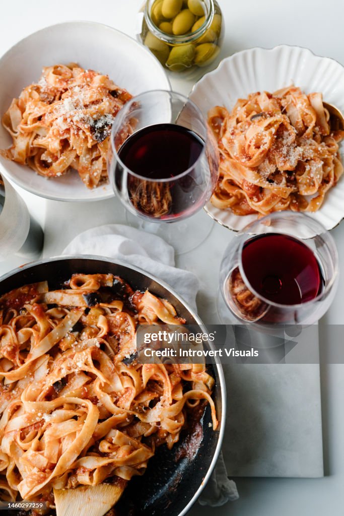 Pasta with tomato sause in a souse pan with glasses of red wine on marble table