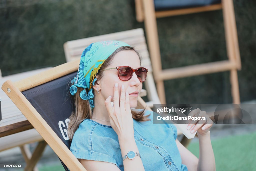 Mid Adult Woman Relaxing At The Beach Cafe And Applying Sunscreen On Her Face