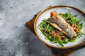 Fried sea bass fillet with vegetable salad, Dicentrarchus fish. Gray background. Top view. Copy space