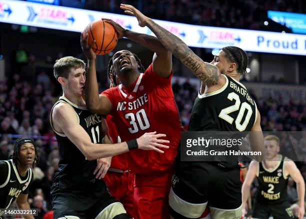 Burns Jr. #30 of the North Carolina State Wolfpack drives between Andrew Carr and Davion Bradford of the Wake Forest Demon Deaconsduring the second...