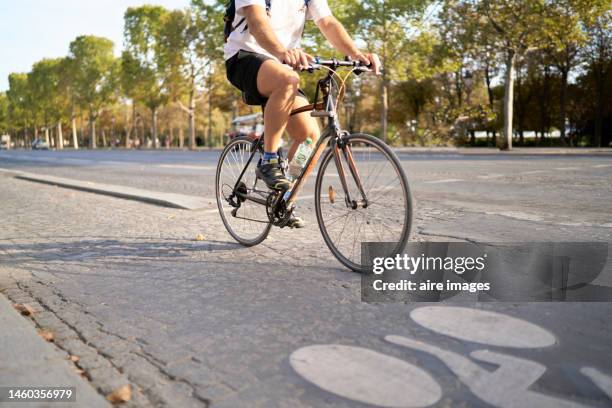 legs of a man in side view riding a bicycle on an avenue in paris carrying a bottle of water, car in the background - day to the liberation of paris photos et images de collection