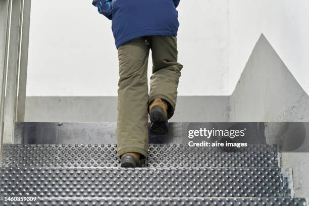 unrecognizable person in jacket climbing a staircase inside a building, low angle rear view - 胴上げ ストックフォトと画像