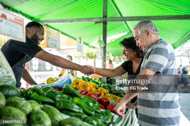 venditore che saluta i clienti su un mercato di strada - mercato di prodotti agricoli foto e immagini stock
