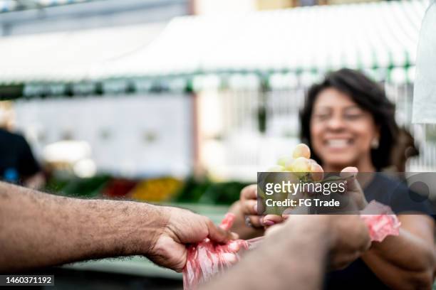 close-up of a human hand putting the grapes bunch in a plastic bag on a street market - grape stock pictures, royalty-free photos & images