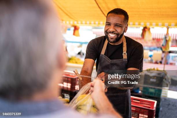 verkäufer hilft seinem kunden, die bananen in eine plastiktüte auf einem straßenmarkt zu stecken - shopping candid stock-fotos und bilder