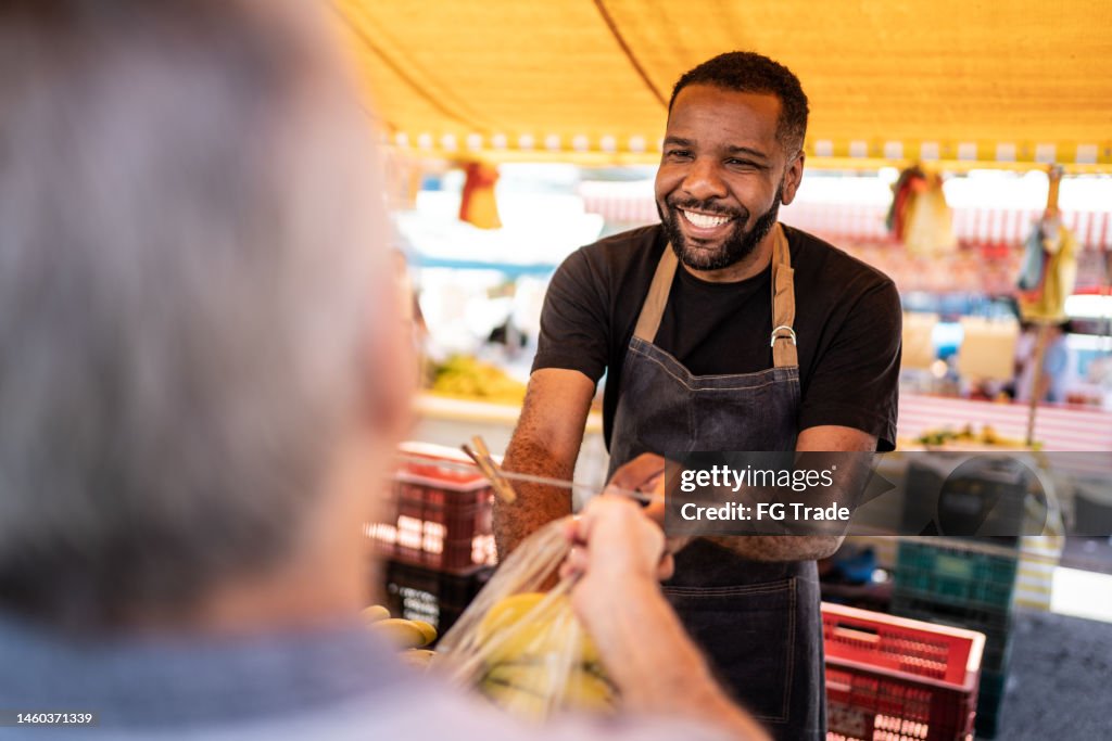Salesman helping the his customer putting the bananas in a plastic bag on a street market