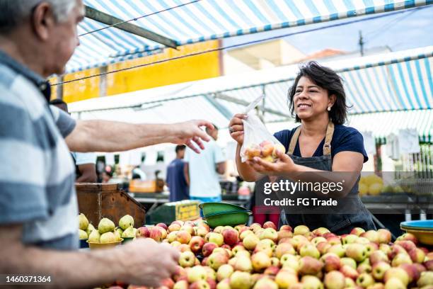 saleswoman giving the fruits bag to her customer on a street market - apple products stock pictures, royalty-free photos & images