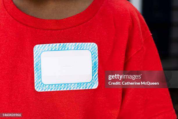 young african-american boy wearing red t-shirt with blank name tag - naamplaatje etiket stockfoto's en -beelden