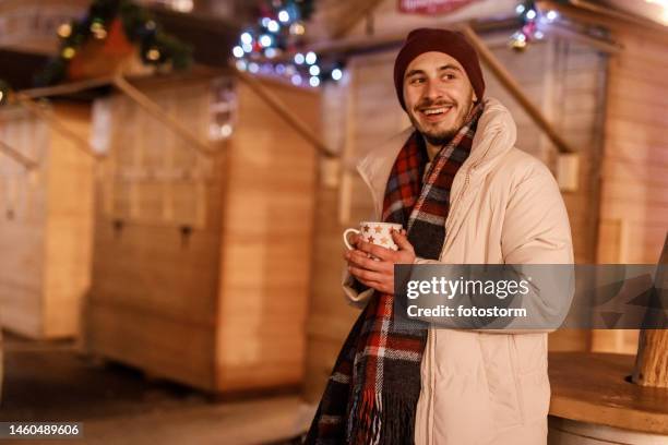 fröhlicher junger mann genießt glühwein auf dem weihnachtsmarkt - punsch stock-fotos und bilder