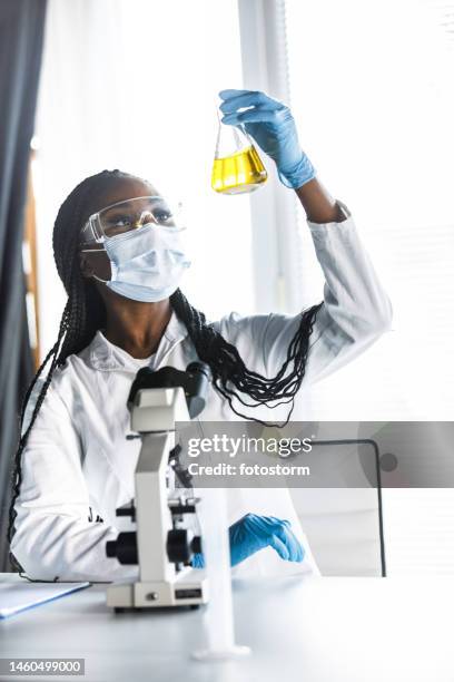 laboratory technician in protective gear analyzing yellow liquid for research - volume fluid capacity stock pictures, royalty-free photos & images