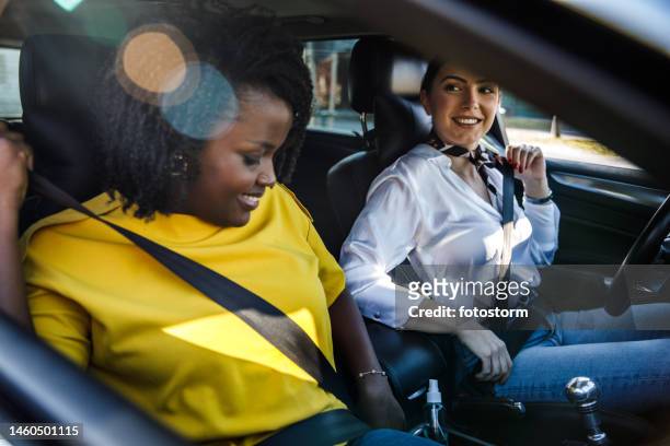 dos amigas sentadas en un coche y abrochándose los cinturones de seguridad antes de salir a dar una vuelta - abrochar fotografías e imágenes de stock