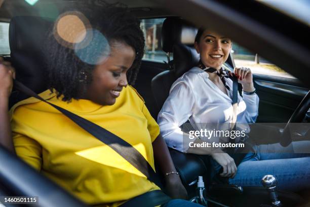 two girlfriends sitting in a car and fastening their seat belts before going for a drive - fastening stock pictures, royalty-free photos & images