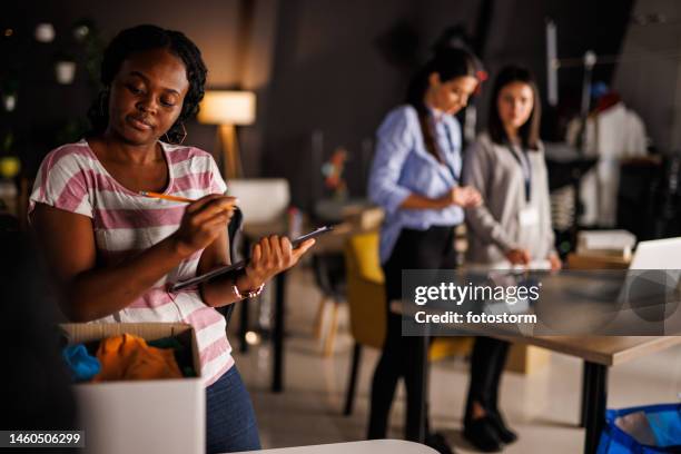 young woman writing a list of clothes for donations that she is sorting out - the fashion institute of technology stock pictures, royalty-free photos & images