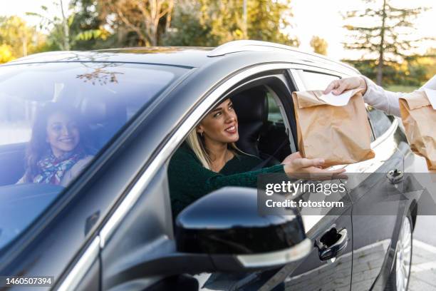 young woman sitting in her car, receiving her takeaway food at the drive through - burger king imagens e fotografias de stock