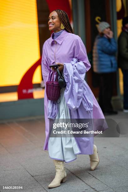 Guest wears a purple ribbed wool turtleneck pullover, a purple oversized belted long shirt dress, a purple rain long coat, a purple wickers handbag,...