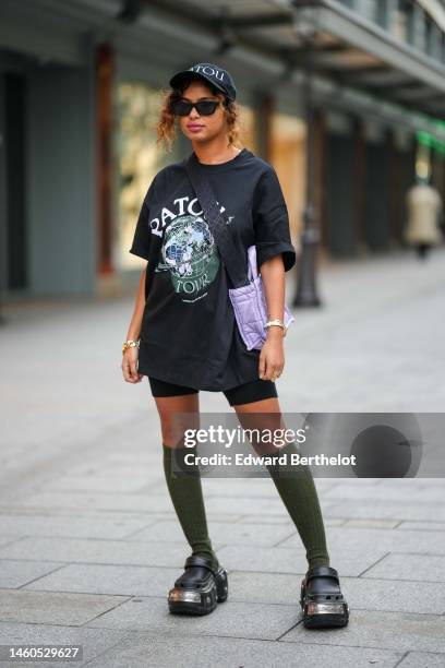 Guest wears a black with white embroidered logo pattern cap, black sunglasses, a black with embroidered pink and green print pattern t-shirt from...
