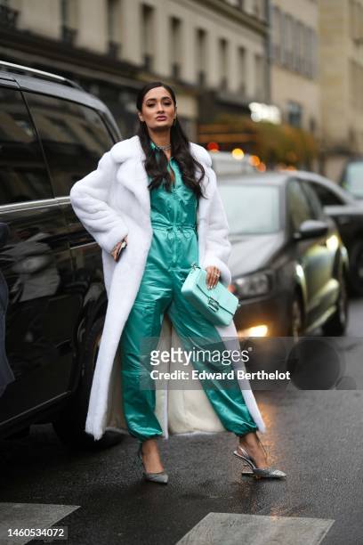 Guest wears a green blue silk jumpsuit from Fendi, a white fur long oversized coat, silver and diamonds earrings, a silver and diamonds necklace,...