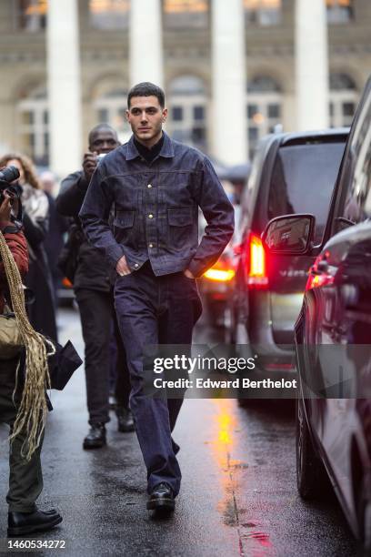 Guest wears a black polo shirt, a navy blue denim buttoned jacket, navy blue denim large pants, black shiny leather zipper ankle boots from Dr...