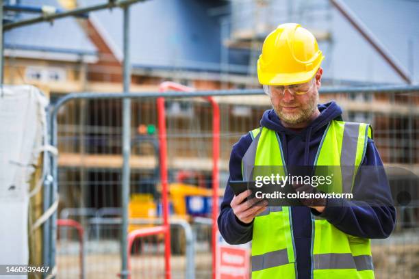 construction worker using digital tablet on building site - mid adult stock pictures, royalty-free photos & images