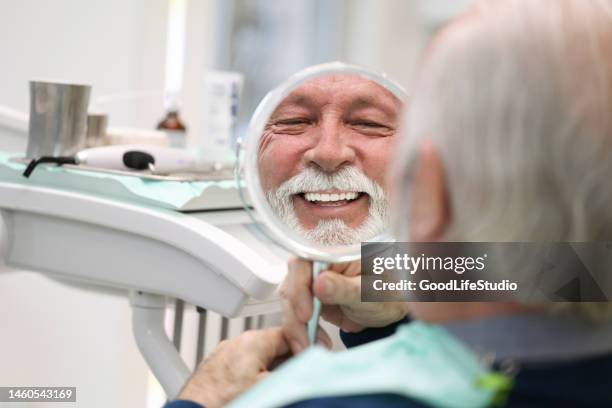 senior man looking in a mirror at a dentist's office - equipamento dentário imagens e fotografias de stock