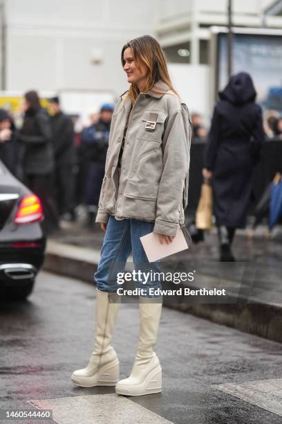 Guest wears a gray denim oversized jacket from Fendi, blue denim cigarette pants, white latte shiny leather wedge heels knees boots / high boots ,...