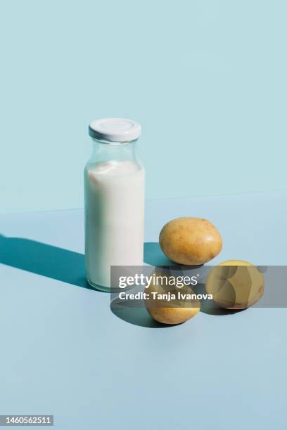 potato milk alternative plant based dairy drink in glass and potato tubers on blue background. healthy vegetarian and vegan drink concept. lactose-free milks in minimal style, copy space. - milk plant stock-fotos und bilder