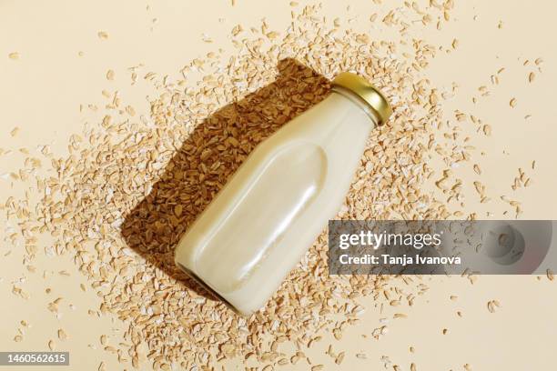 oat milk in glass bottle and oatmeal flakes on beige background. healthy vegan non-dairy organic drink with flakes. lactose-free milks in minimal flat lay style. top view. - oat stock pictures, royalty-free photos & images