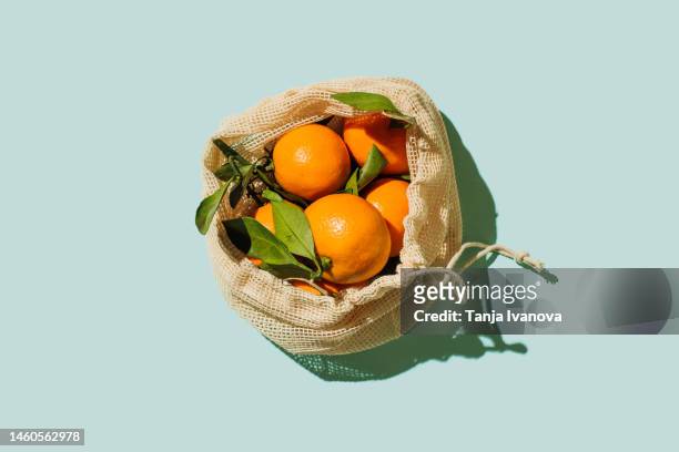 fresh mandarins tangerines or clementines in a reusable white cotton bag on blue background. sustainable lifestyle. eco friendly, zero waste, plastic free concept. healthy clean eating diet and detox. - reusable bag isolated stock pictures, royalty-free photos & images