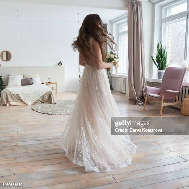 a beautiful young bride in a wedding dress and flowers walks through a room with a beautiful interior. woman in the long dress in the full length. lifestyle with copy space. - white dress back stock pictures, royalty-free photos & images